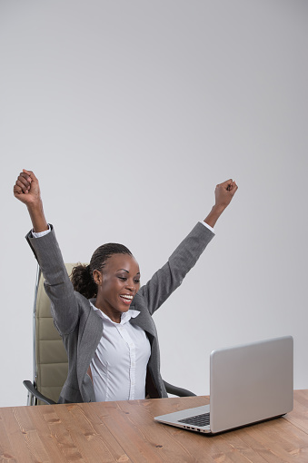 Successful business woman with arms up sitting in front of laptop at office